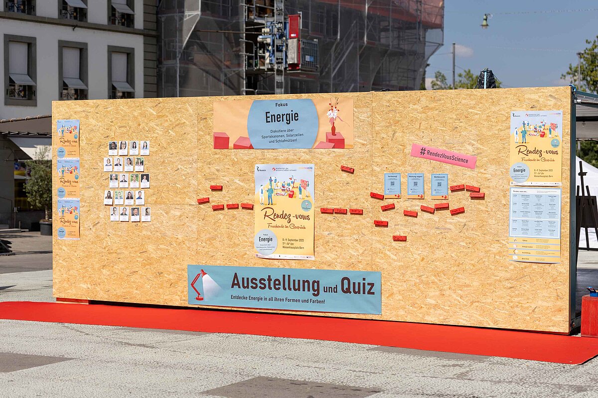 Eine Holzwand mit Namen, Plakaten und Fotos